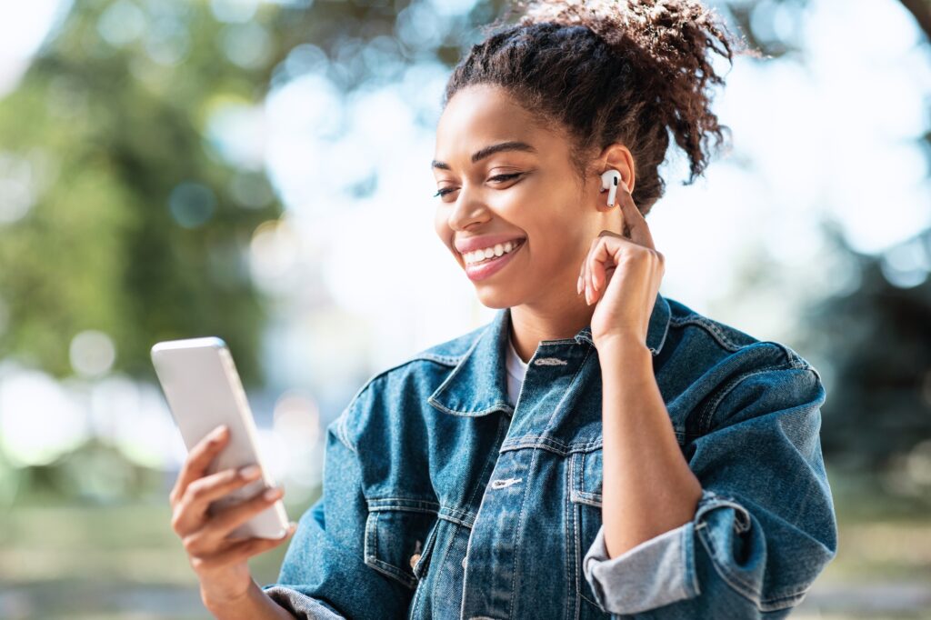 african woman using cellphone and earbuds making video call outdoors