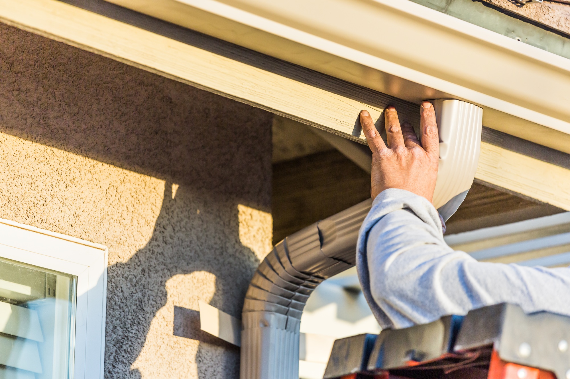 worker attaching aluminum rain gutter and down spout to fascia of house